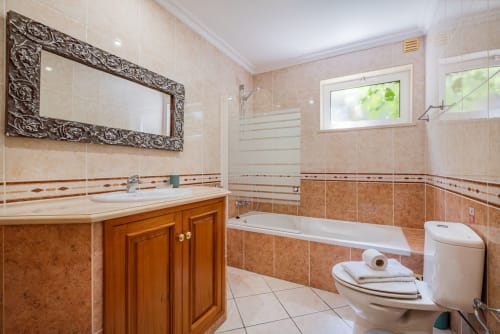 Banheiro luxuoso na Villa Rosal, Albufeira com penteadeira em madeira, espelho ornamentado e banheira com chuveiro moderno