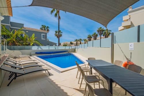 Área de piscina da Villa Rosal by SignatureStays em Albufeira com espreguiçadeiras, mesa de refeições e palmeiras