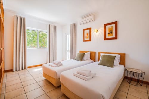 Quarto duplo na Villa Rosal by SignatureStays em Albufeira com duas camas individuais, cabeceiras laranja e comodidades modernas