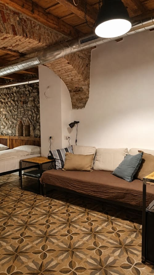 Modernes Loft-Hotel-Zimmer in Bergamo mit Sichtmauerwerk, weißen Wänden, Bett, Sofa mit Kissen, Holzboden
