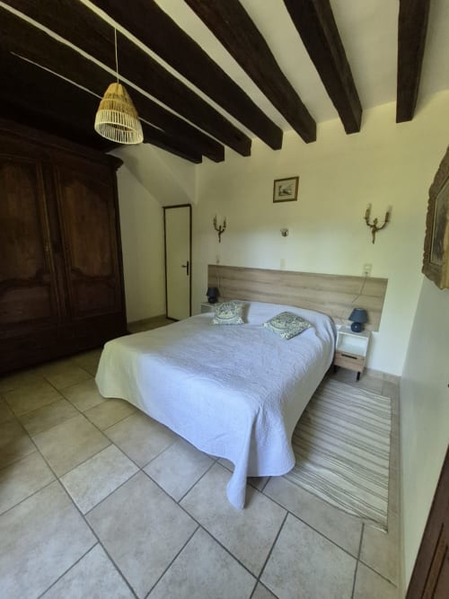 Spacieuse chambre de la maison d'hôtes Le Moulin Garnier avec poutres apparentes, lit queen-size et carrelage en terre cuite