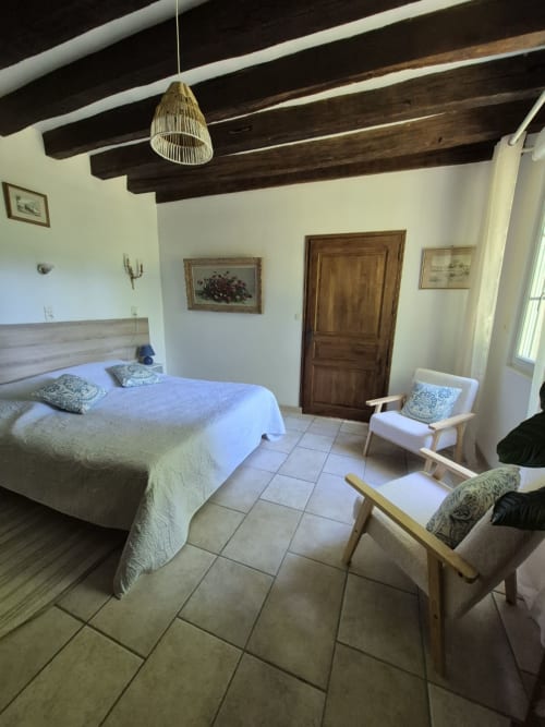 Chambre spacieuse au Moulin Garnier avec lit queen, poutres apparentes, lampe suspendue et coin détente avec vue