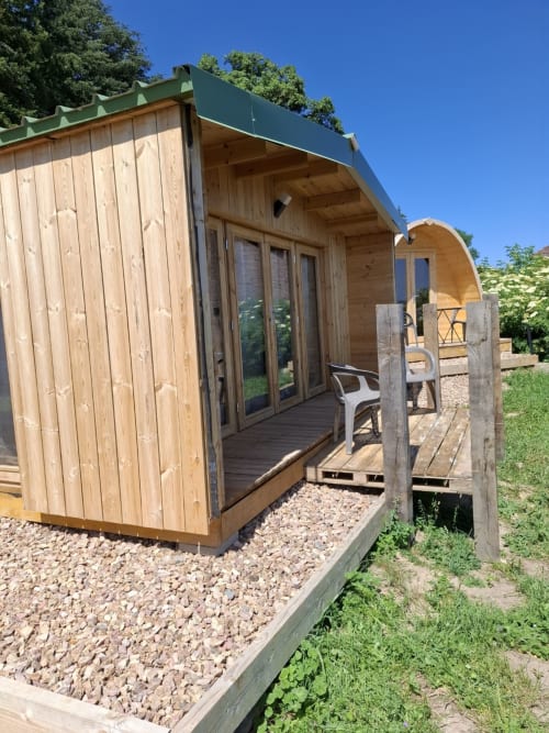 Modern wooden glamping pod with green roof at La Maison de Dun, Saint Racho, featuring deck and gravel pathway