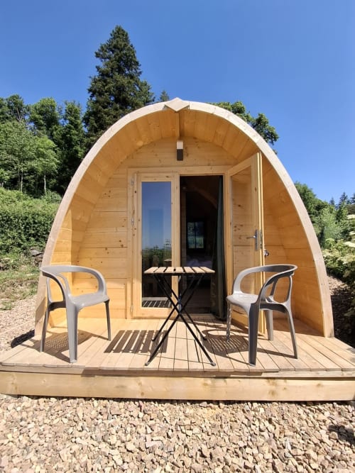 Wooden pod cabin at La Maison de Dun with deck, chairs, and forest backdrop in Saint Racho