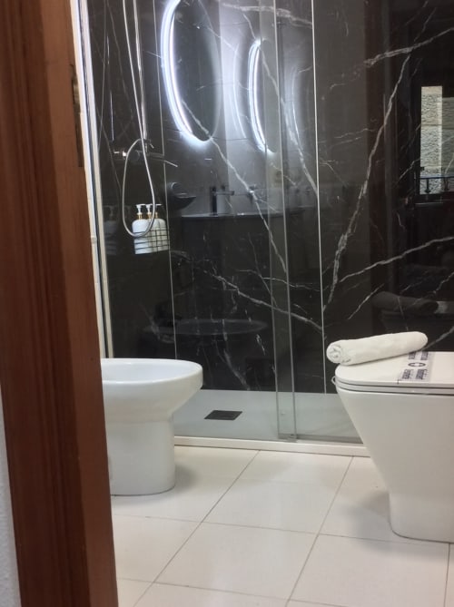 Cuarto de baño moderno en Houses by Pilar, Arcade España con ducha abierta, muros de mármol, iluminación neón, accesorios blancos y calefacción