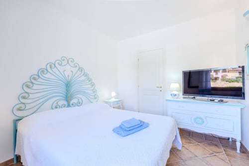 Camera luminosa con testata decorativa pavone, letto bianco, TV a schermo piatto e pavimenti in cotto presso Perseo Case Vacanze