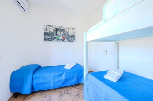 Camera luminosa nella villa Olba con letti blu, pareti bianche e vista sulla piscina dalla finestra