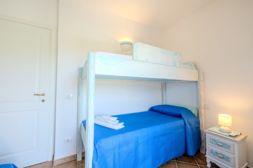 Camera luminosa nella villa Poggio dei Fiori di Olbia con letto a castello in legno bianco, biancheria blu e comodino con lampada