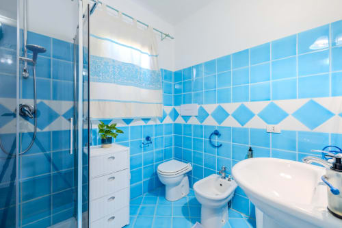 Bagno luminoso con piastrelle blu nella villa Poggio dei Fiori di Olbia, completo di doccia, WC, bidet e lavabo