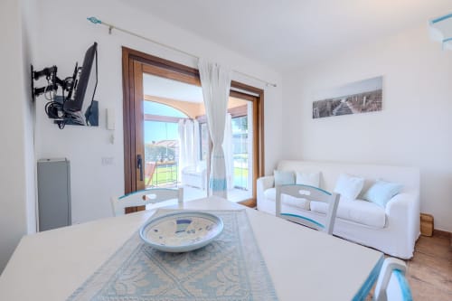 Luminoso soggiorno moderno nella villa Poggio dei Fiori, Olbia, con divano bianco, tavolo da pranzo e vista piscina dalla terrazza