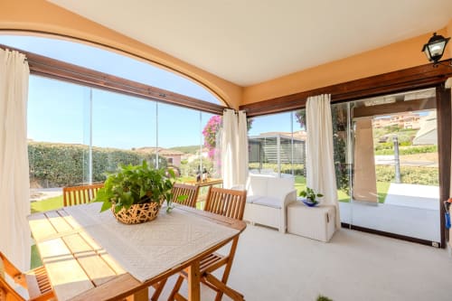 Terrazza coperta soleggiata della villa Poggio dei Fiori a Olbia con tavolo da pranzo in legno, sedie e vista giardino