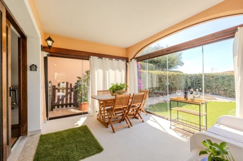 Portico della villa al sole con tavolo da pranzo in legno, sedie e vista sul giardino a Poggio dei Fiori a Olbia