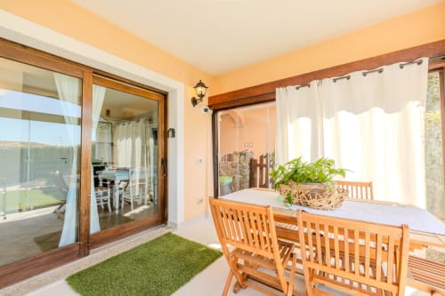 Terrazza soleggiata a Villa Poggio dei Fiori a Olbia con sedie in legno, piante in vaso e vista sulla piscina