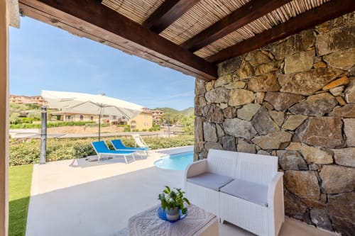Terrazza ombreggiata della villa Poggio dei Fiori a Olbia con divano in rattan bianco, muro in pietra e vista piscina