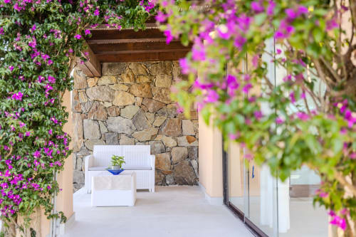 La vibrante buganvillea rosa incornicia il patio in pietra con sedute bianche della villa Perseo Case Vacanze a Olbia