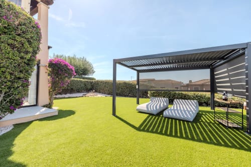 Soleggiato giardino della villa Poggio dei Fiori a Olbia con lettini a righe sotto moderna pergola