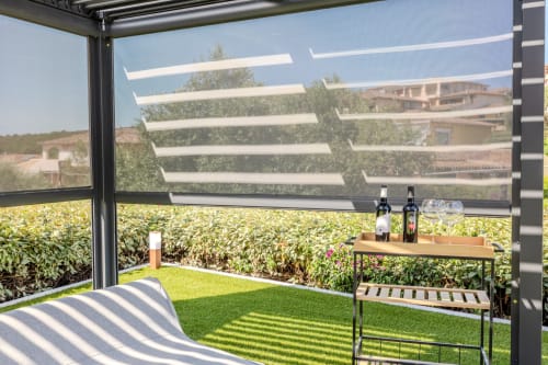 Terrazza ombreggiata della villa Poggio dei Fiori a Olba con prato verde, bottiglie di vino, tavolo da pranzo e vista sul giardino