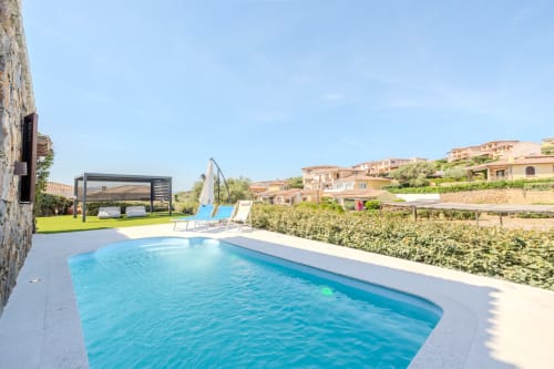 Piscina con lettini presso villa Poggio dei Fiori a Olbia, circondata da giardini curati e terracotta