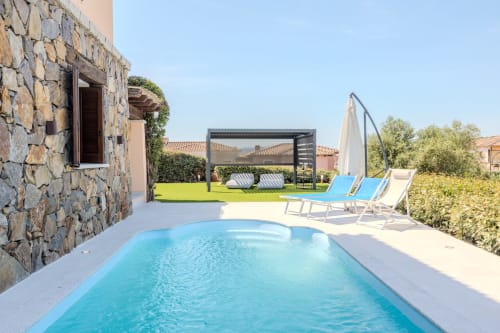 Piscina di Villa Poggio dei Fiori con lettini, pergola e edificio in pietra a Olbia, Italia