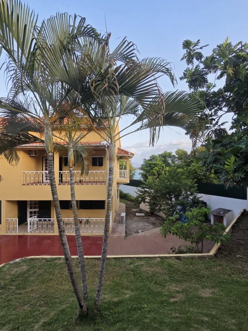 Casa colorida em amarelo e vermelho com vários andares, palmeiras, gramado verde e vista para o oceano no Equador