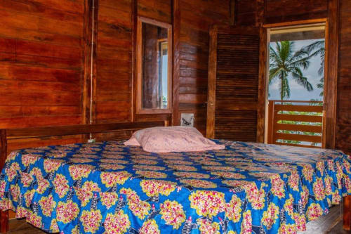 Quarto de cabana de madeira na Ecuador Houses com colcha floral azul, vista de palmeira pela porta da varanda