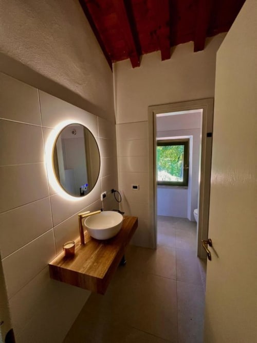 Modernes Badezimmer in der Villa Blu am Prince Garda, Salò mit beleuchtetem Spiegel, weißem Aufsatzwaschbecken und Holzwaschtisch