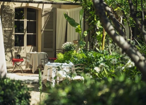 Cour de jardin isolée aux Jardins de Baracane à Avignon avec végétation luxuriante, petites tables et portes-fenêtres