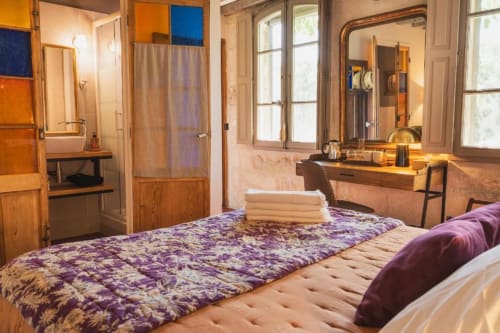 Chambre élégante avec literie à motifs violets, mobilier en bois et salle de bain attenante aux Jardins de Baracane à Avignon