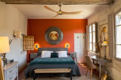 Chambre moderne de la maison d'hôtes d'Avignon avec mur accent orange éclatant, lit sombre, ventilateur de plafond en bois et vue sur le jardin