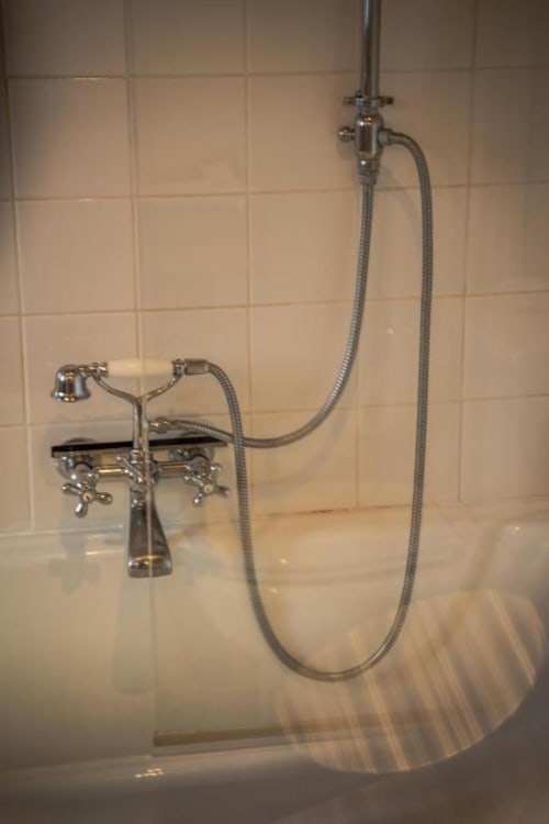 Robinetterie de baignoire style vintage avec douchette à main dans une salle de bains carrelée de crème aux Jardins de Baracane Avignon