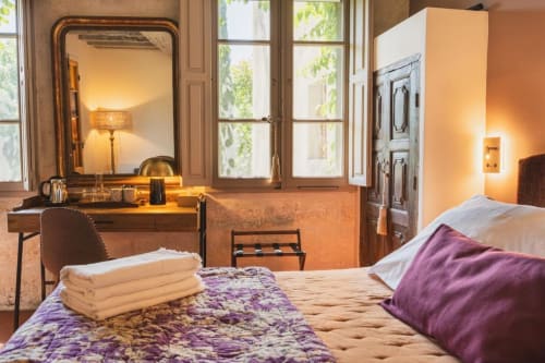 Chambre élégante aux Jardins de Baracane, Avignon avec literie violette, miroir de coiffeuse et éclairage ambiant chaleureux