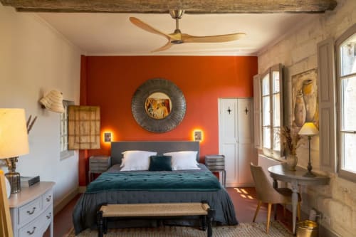 Chambre chaleureuse aux Jardins de Baracane Avignon avec mur d'accent orange, lit sombre et poutre en bois rustique
