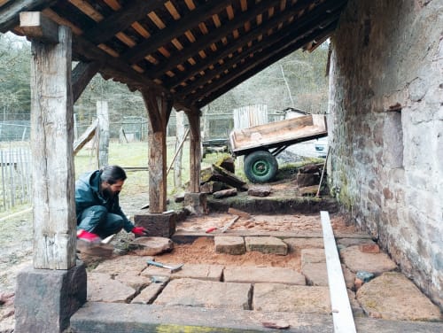 Personne travaillant sur un chemin de pierre rustique sous une structure en bois à la Paulusmühle B&B à Soucht, France