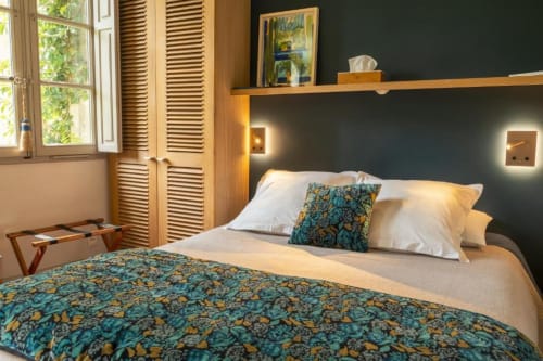 Chambre élégante aux Jardins de Baracane avec literie turquoise à motifs, oreillers blancs, mur d'accent sombre et jardin