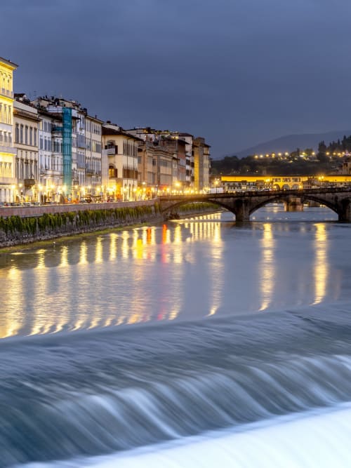 Fiume Arno al tramonto con edifici rinascimentali illuminati e ponte in pietra a Firenze, Italia