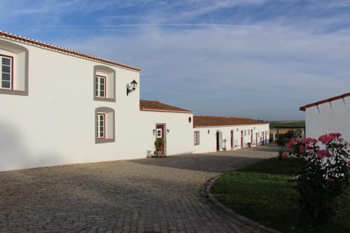Pátio da Quinta Monte da Morena em Serpa com edifícios caiados, telhas de barro e arbustos com flores cor-de-rosa