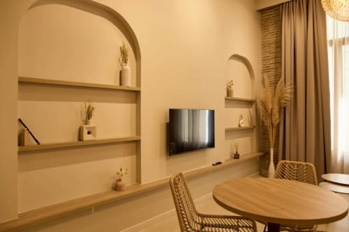 Habitación moderna del hotel Arrels Mercat Valencia con TV en pared, estanterías arqueadas, mesa de madera y sillas tejidas en tonos cálidos