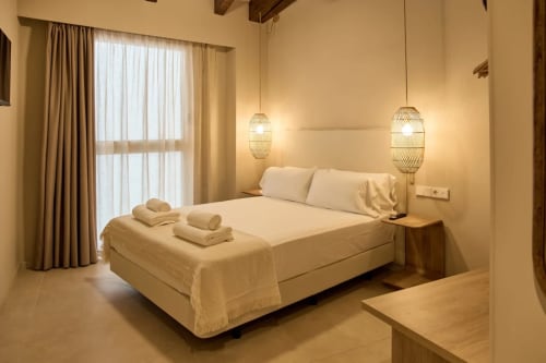 Dormitorio moderno en el hotel Arrels Mercat de Valencia con cama de matrimonio, iluminación colgante, decoración crema y acceso a balcón
