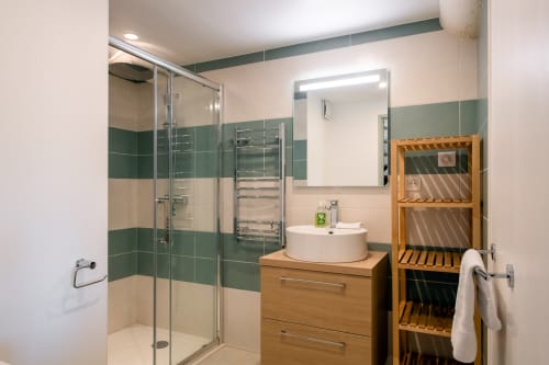 Salle de bain moderne de l'appartement St Eloi à Villeneuve les Avignon avec carrelage vert et beige, douche à l'italienne, finitions bois