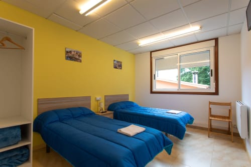 Luminosa habitación doble en Hostal A Taberna de Vento en Lalín con dos camas azules, pared amarilla y luz natural desde