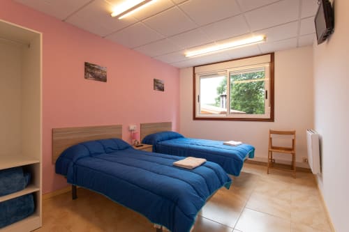 Luminosa habitación doble en el Hostal A Taberna de Vento de Lalín con dos camas azules, paredes rosa y suelos de madera