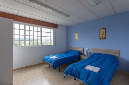 Luminosa habitación doble azul en Hostal A Taberna de Vento en Lalín con dos camas, grandes ventanales y muebles de madera