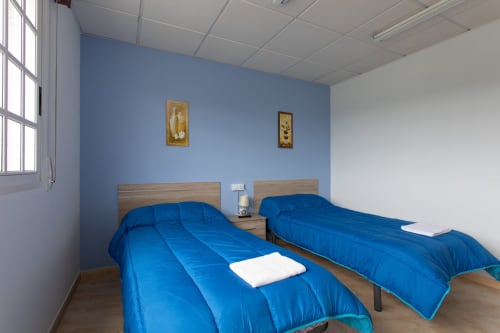 Luminosa habitación doble con dos camas azules en Hostal A Taberna de Vento en Lalín, pared acentuada azul y luz natural
