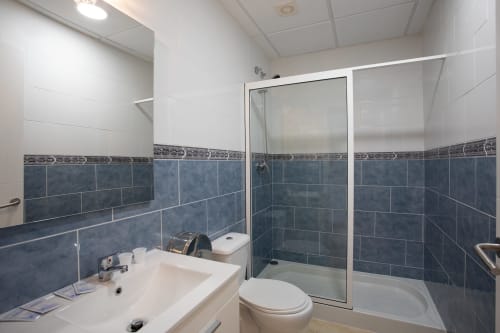 Baño moderno con azulejos azules, lavabo blanco, inodoro y ducha con mampara de cristal en Hostal A Taberna de Vento en Lalín