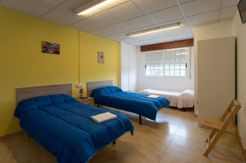 Habitación triple en Hostal A Taberna de Vento en Lalín con dos camas azules, paredes amarillas y luz natural desde la ventana