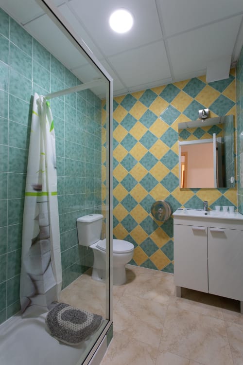 Cuarto de baño moderno en el Hostal A Taberna de Vento en Lalín con azulejos de diamantes turquesas y amarillos, ducha, inodoro y lavamanos