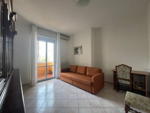 Luminoso soggiorno nell'appartamento di Forlì con divano arancio, accesso alla terrazza in cotto, climatizzatore e arredi moderni