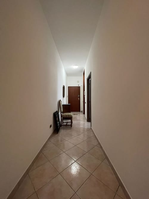 Lungo corridoio con pareti bianche, pavimento piastrellato e porte in legno nell'appartamento LHE, Forlì