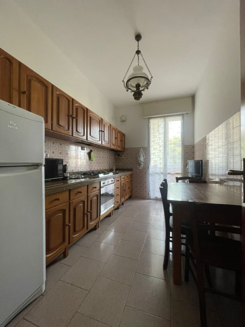 Ampio living-cucina nell'appartamento di Forlì con arredamento in legno, elettrodomestici bianchi e tavolo da pranzo