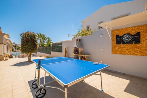 Mesa de ping pong azul em pátio ensolarado na Signature Stays Portugal com edifícios brancos e palmeiras